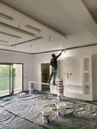 A worker painting the interior wall and ceiling of a room