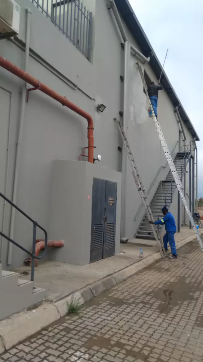 Two workers painting the exterior wall of a building using ladders