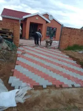 Workers laying red and grey interlocking pavers for a driveway