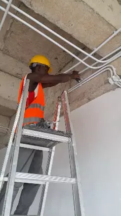 Construction worker on a ladder installing electrical conduits on a ceiling