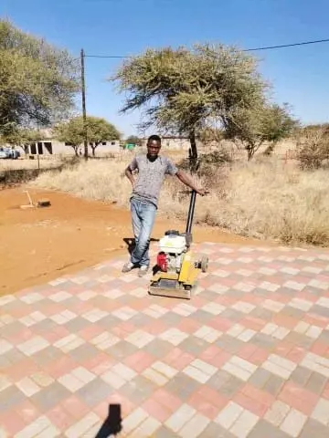 A man standing next to a plate compactor on a newly paved area
