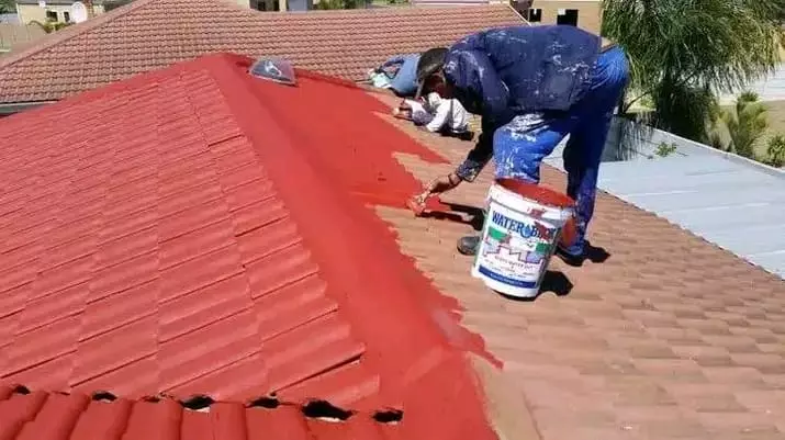 Worker painting a tiled roof red